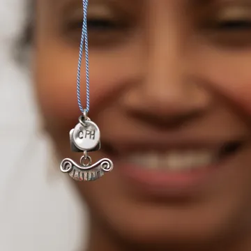 Ciondolo d'argento con scritta CPH davanti al volto sorridente sfocato di una donna